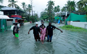 Police and rescue personnel evacuate a local resident through a flooded street in a coastal area after heavy rains under the influence of cyclone 'Tauktae' in Kochi on May 14, 2021.