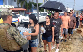 A Coast Guard member deployed to Borinquen, Puerto Rico in support  of Hurricane Maria relief efforts delivers a case of water to a resident of Moca, Puerto Rico, Oct. 9, 2017.