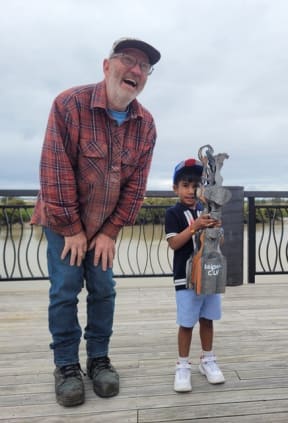Sculptor Jeff Thomson presents a corrugated iron trophy to the winner of the 2024 Kaipara River paper boat race.