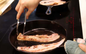 Two slices of bacon being cooked on a frying pan.