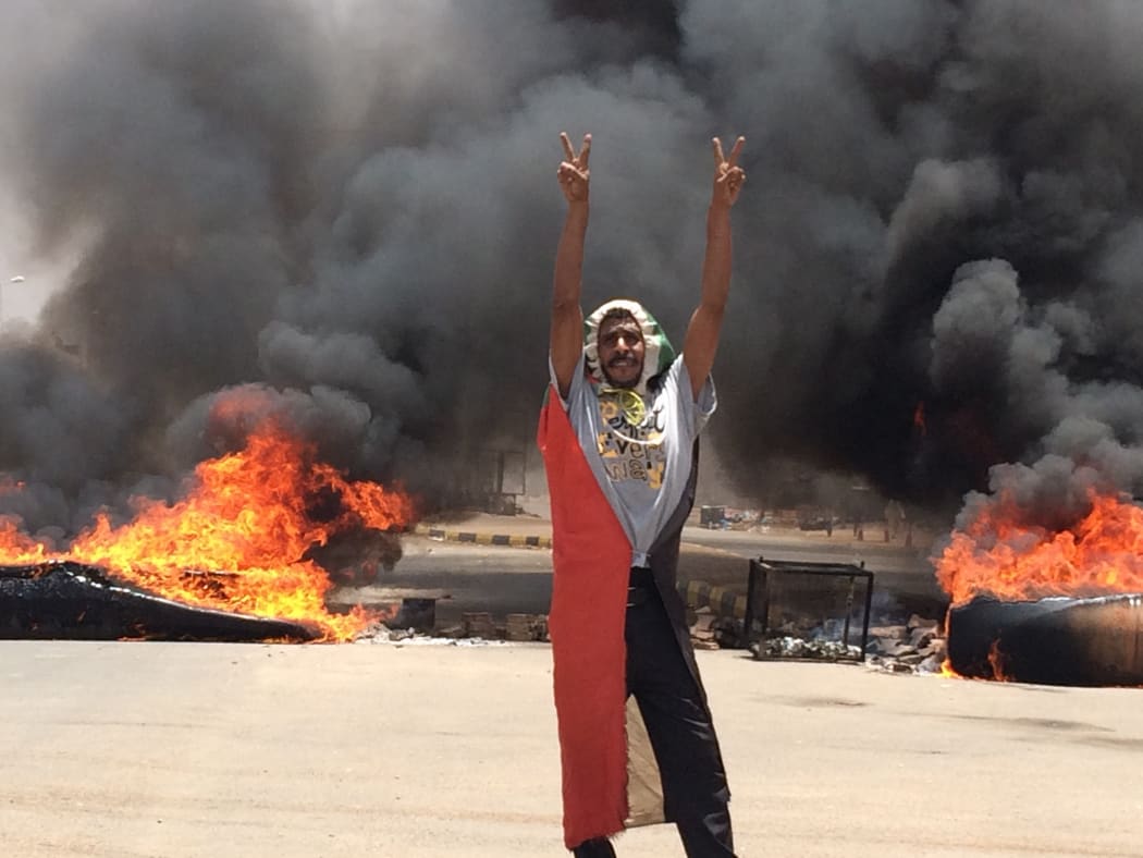 A protester in front of burning tires and debris on the road near Khartoum's army headquarters.
