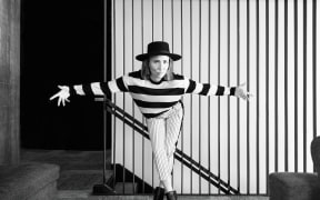 A black and white photo of singer songwriter KT Tunstall wearing stripey clothing, bowing in front of a striped wall.