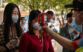 A worker wearing a face mask checks passengers body temperatures and a health code on their phones before they take a taxi after arriving at Hankou railway station in Wuhan, China's central Hubei province on May 12, 2020.