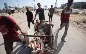 Palestinians transport a man, wounded as he waited for humanitarian aid at a GHF aid distribution point, at the entrance of the Bureij refugee camp in the central Gaza Strip on 30 July, 2025.