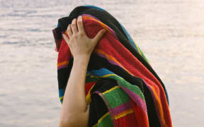 A man hides behind a towel.