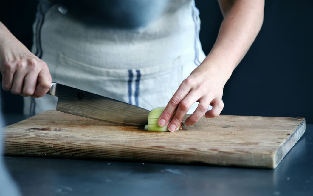 A person chops a cucumber on a wooden chopping board.