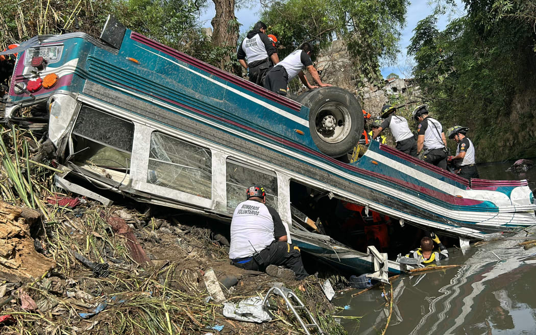Volunteer firefighters work at the scene of an accident in which a bus fell down a ravine in Guatemala City on February 10, 2025. A bus carrying 75 people plunged into a ravine in Guatemala City on Monday, killing at least 31 people, rescue workers said. (Photo by Johan ORDONEZ / AFP)