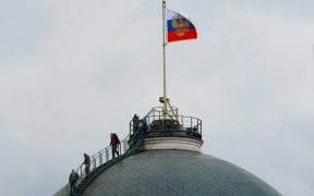 People gather on the dome of the Senate Palace -- topped with the Russian flag -- which is one of the main buildings within the Kremlin compound, in central Moscow on May 3, 2023. - Russia said on May 3, 2023 it had shot down two drones aimed at President Vladimir Putin's Kremlin residence in what it called a Ukrainian "terrorist" assassination attempt.