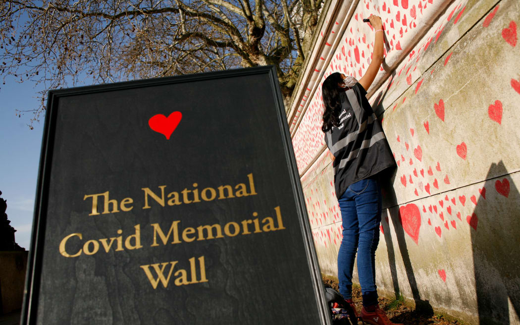 A woman draws red hearts representing individual coronavirus deaths onto the National Covid-19 Memorial Wall in London, England, on March 30, 2021.