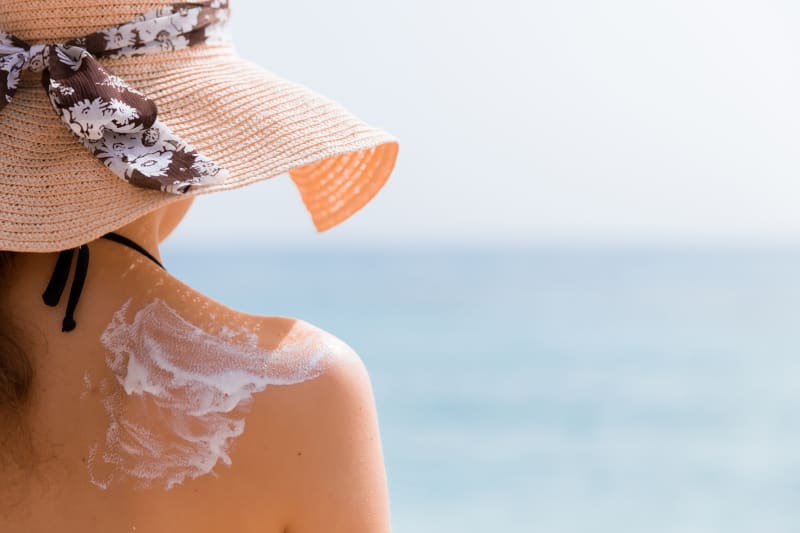 Young girl in straw hat applying sunscreen on her back to protect her skin.