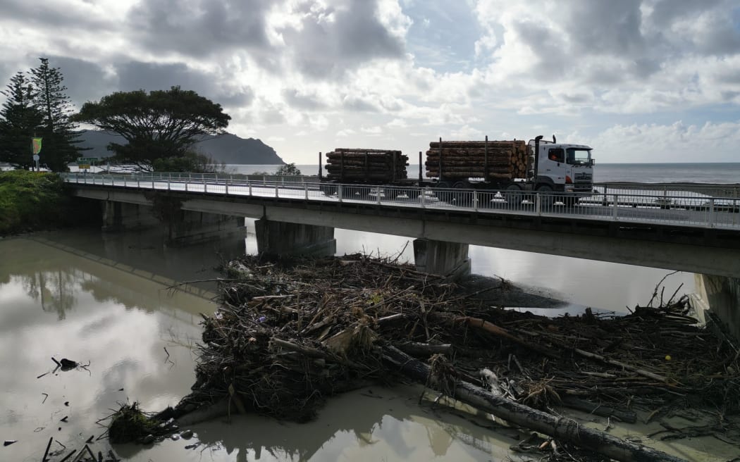 Logging truck crossing a bridge in Tokomaru Bay with slash in the river.
