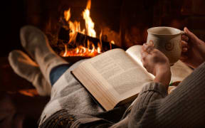 woman with mug and book by the fire
