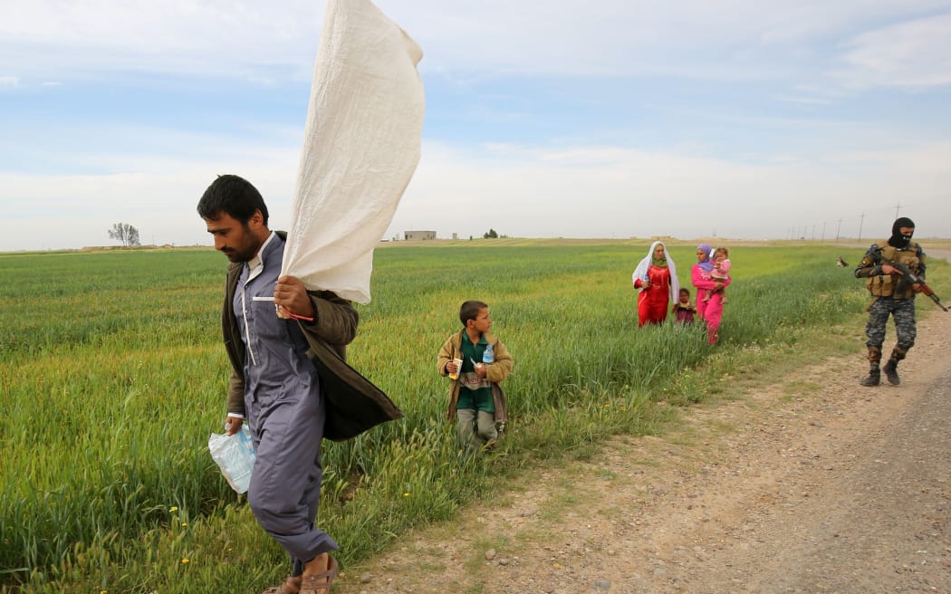 An Iraqi man carries a makeshift white flag as he flees the fighting with his family.