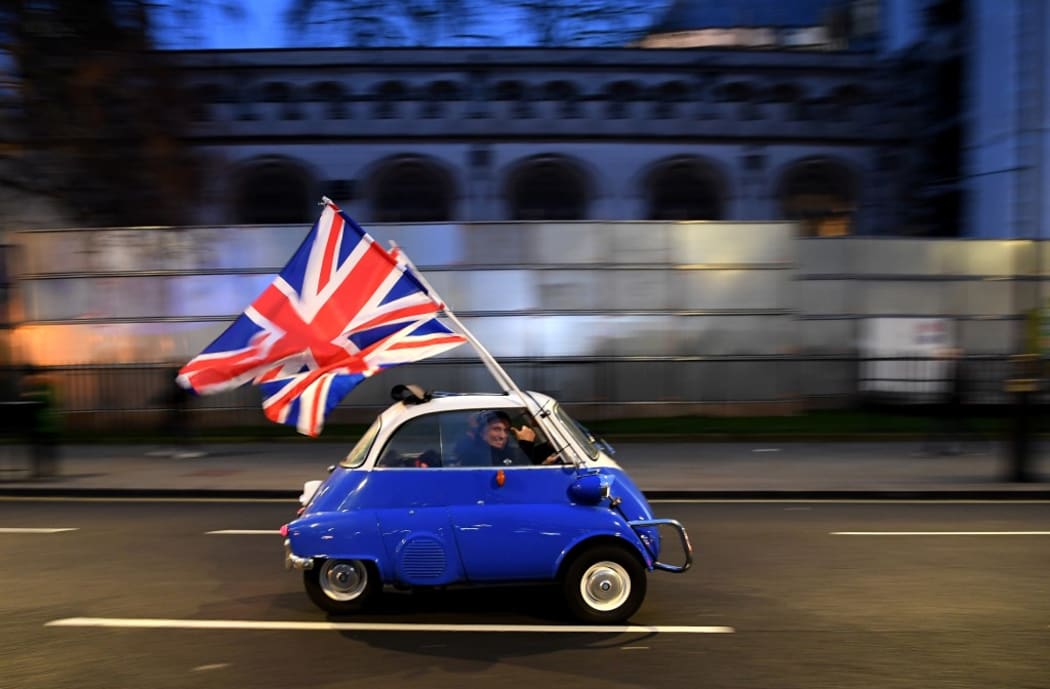 A man waves Union flags from a BMW Isetta as he drives past Brexit supporters gathering in Parliament Square, in central London on January 31, 2020, the day that the UK formally leaves the European Union