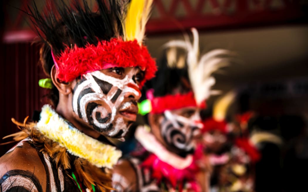 A line of men in feather headress with black and white face decorations