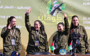 Four Israeli hostages wave on a stage before Hamas fighters hand them over to a team from the Red Cross in Gaza City on January 25, 2025. Hamas militants handed over four Israeli women hostages to the Red Cross in a January 25 swap after parading them on a stage at a square in Gaza, an AFP journalist reported. (Photo by Omar AL-QATTAA / AFP)
