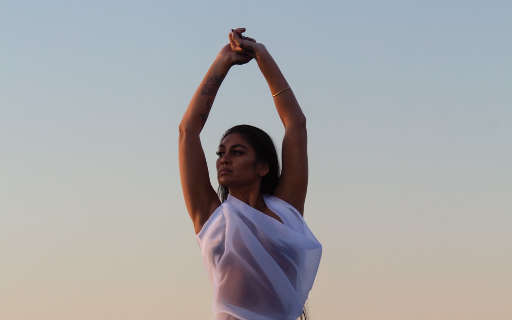 The album cover for 'Sweet Surrender'. Singer/songwriter Aaradhna poses against the background of the setting sun at the beach. Her arms in the air.
