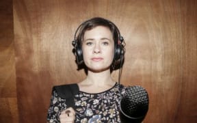 A portrait of Bang! presenter Melody Thomas, thrusting a microphone towards the camera.