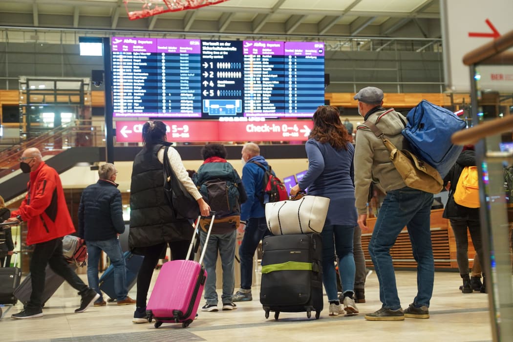 Travellers stand in front of an information board at BER Airport.