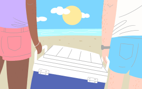 Two people carrying a chilly bin at the beach
