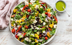 A round platter of containing Mexican black bean and corn salad with coriander dressing, with a small bowl of green dressing to the side.