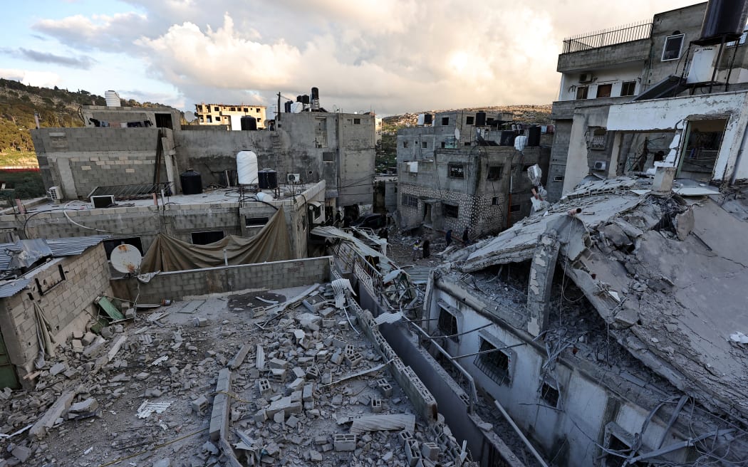People stand amid the rubble of a building destroyed during an Israeli raid at the Nur Shams camp for Palestinian refugees near the occupied West Bank city of Tulkarm, on 4 January, 2024.