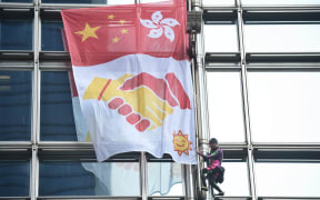 French urban climber Alain Robert, popularly known as the French Spiderman, secures a banner, showing shaking hands below a depiction of the Chinese and Hong Kong flags, during his ascent of the Cheung Kong Center building in Hong Kong on August 16, 2019.