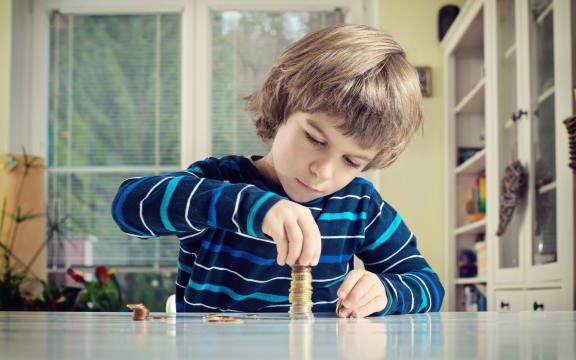 A photo of a little boy making stack of coins, counting money at table. Learning financial responsibility and planning savings concept.
