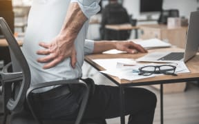 Employer having pain in back. He holding it by hand while sitting at table during job. Worker with bad state of health concept