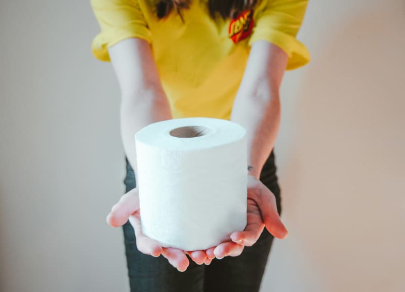 A person holds out a roll of toilet paper.