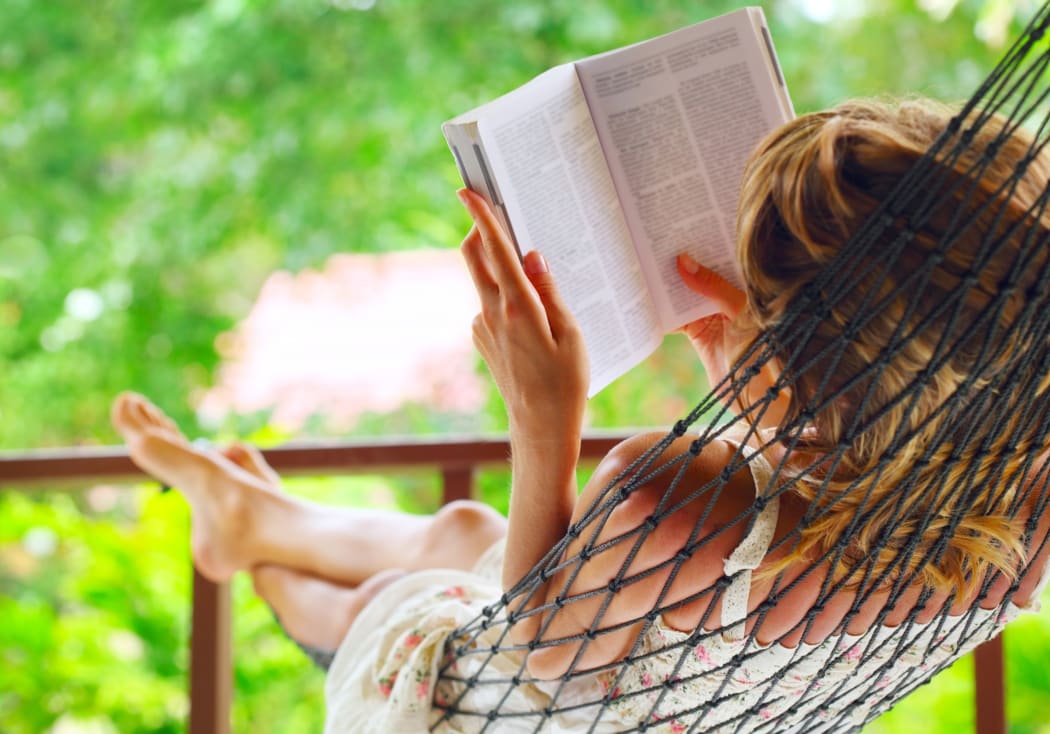9912221 - young woman lying in hammock in a garden and reading a book. shallow dof. focus on a left shoulder