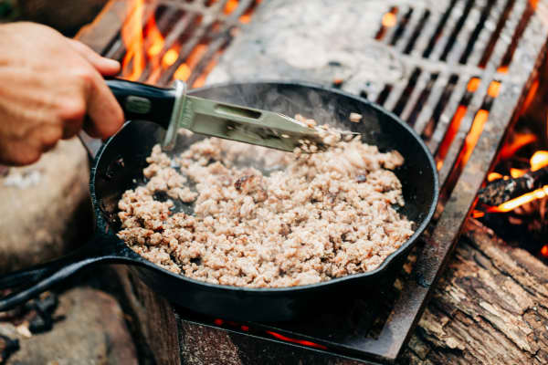 A cast iron pan with minced meat being cooked outdoors on barbecue grill.