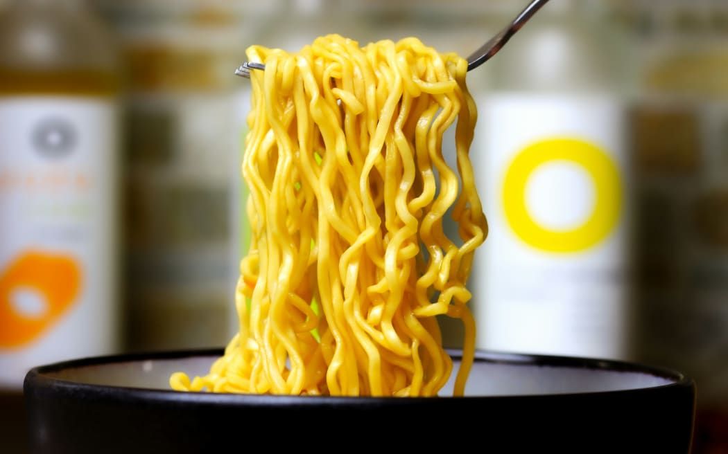 Fork holding up some cooked instant noodles from a bowl.