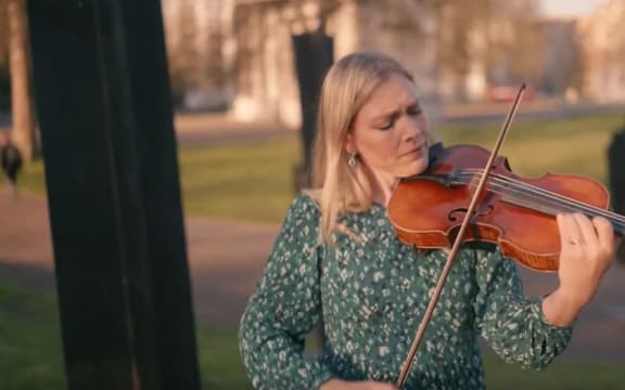 A woman plays the viola in a park.
