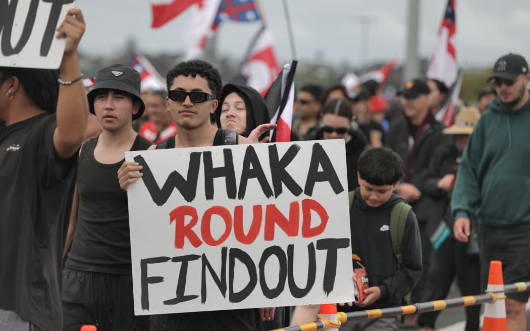 A man holds a strongly worded sign as he crosses the Auckland Harbour Bridge on the hīkoi.