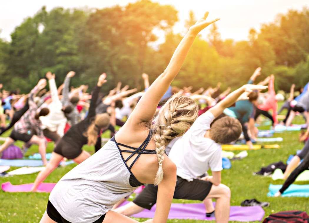 A big group of adults attending a yoga class outside in park