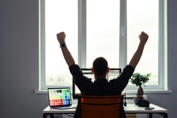 A person stretching at a desk, with arms raised above their head and their back to the camera.