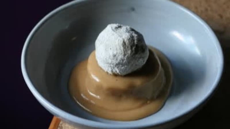 A bowl containing a sugary, deep fried feijoa on a bed of custard.
