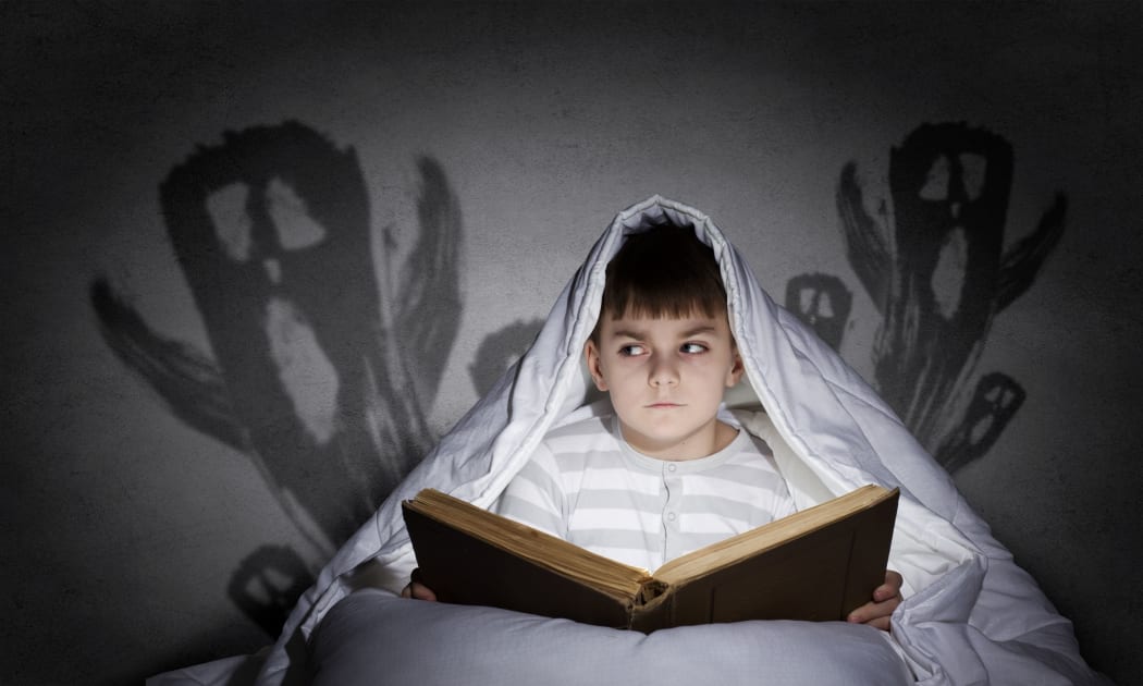 A photo of a boy reading in bed with images of ghosts behind him
