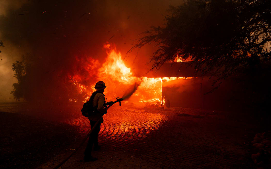 A firefighter tries to control the fire burning down a house as the Mountain Fire scorches acres, the wildfire fueled by strong Santa Ana winds, in Camarillo, California, on November 6, 2024. - A wildfire fanned by powerful winds was burning out of control near Los Angeles on Wednesday, with scores of residents ordered to evacuate and some taken to the hospital. Multiple large homes were destroyed as the fire tore through neighborhoods, blanketing a huge area in thick, choking smoke. (Photo by ETIENNE LAURENT / AFP)
