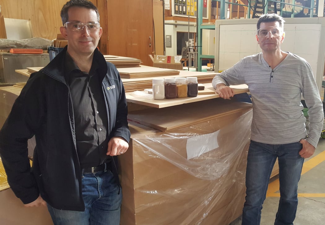 Rob Lei and Warren Grigsby. The raw ingredients for the bioadhesive are in the jars sitting on top of an industrial run of fibreboard manufactured using the new green glue.