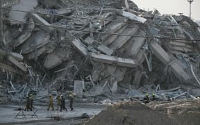 Rescue workers walk past debris of a construction site after a building collapsed in Bangkok on March 28, 2025, following an earthquake. A powerful earthquake rocked central Myanmar on March 28, buckling roads in capital Naypyidaw, damaging buildings and forcing people to flee into the streets in neighbouring Thailand. (Photo by Lillian SUWANRUMPHA / AFP)