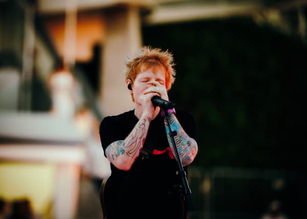 Ed Sheeran covers his face as he sings into a microphone.