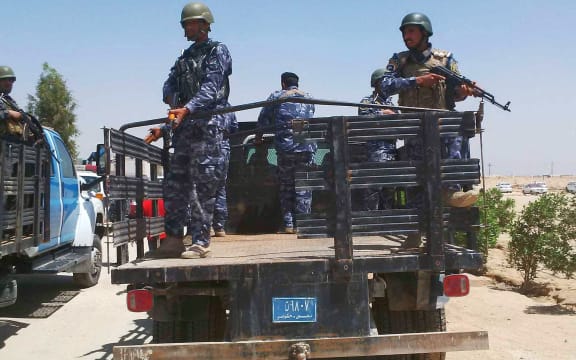 Armed oil police in blue camouflage uniforms on back of flat bed truck.