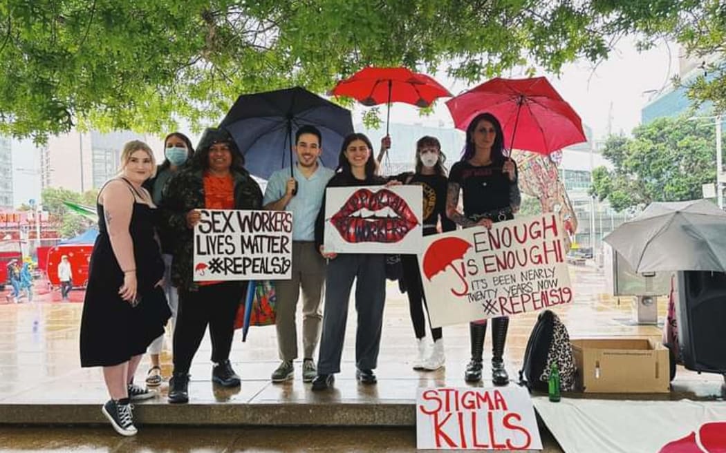 A group shot of people at a sex workers rights protest. They are holding signs with slogans like 'Stigma kills' and 'Sex workers lives matter'.