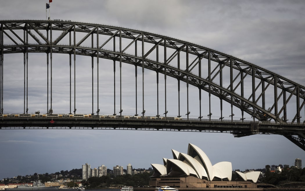 People stand atop of the Sydney Harbour Bridge as ferries sail past the Sydney Opera House during summer on February 11, 2025. (Photo by DAVID GRAY / AFP)