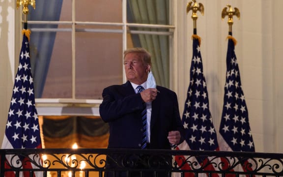 US President Donald Trump takes off his facemask as he arrives at the White House on 5 October, on his return from Walter Reed Medical Center, where he underwent treatment for Covid-19.
