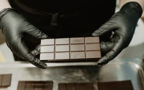 A bar of Solomons Gold Chocolate held by someone in black gloves