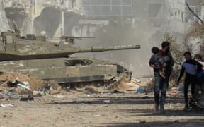 A grab from an AFPTV video shows an Israeli armoured vehicle rolling past Palestinians fleeing Gaza City on foot amid ongoing battles between Israel and the Palestinian Hamas movement on 18 November.