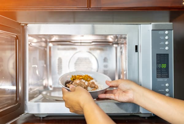 Woman putting bowl food into microwave oven. inside view